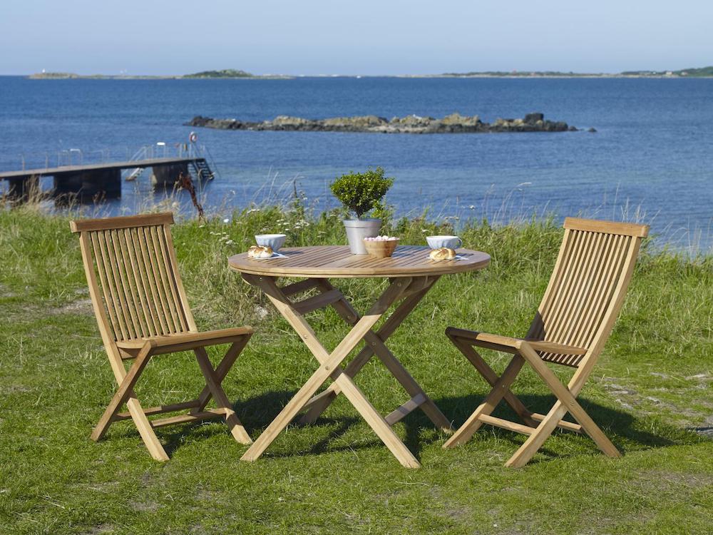 Cafémöbler i trä som står på en gräsmatta med havet i bakgrunden